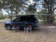 Dark blue SUV with 30 Second 180 Degree Wing Awning and camping chairs setup