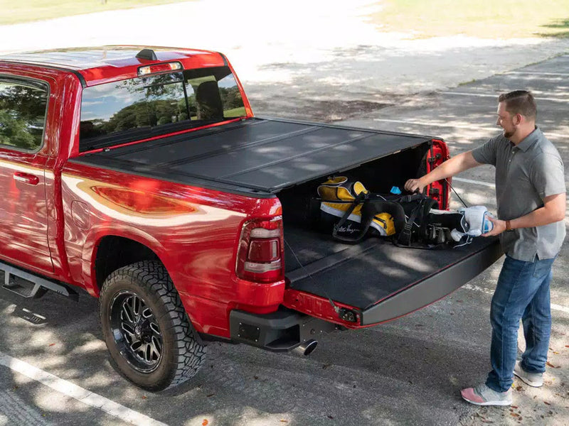 Man loading gear into a red RAM 1500 with the BAKFlip MX4 cover partly folded
