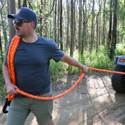 Orange carbon offroad kinetic recovery rope held in a wooded area for offroad recovery