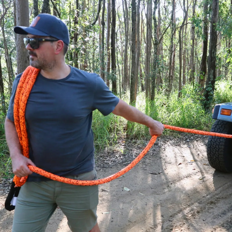 Orange carbon offroad kinetic recovery rope held in a wooded area for offroad recovery