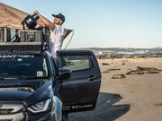 Person on black Isuzu D-MAX with Front Runner Slimline II roof rack kit at beach