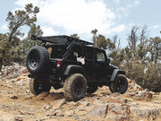 Black Jeep Wrangler with oversized tires on rocky terrain featuring Front Runner roof rack kit