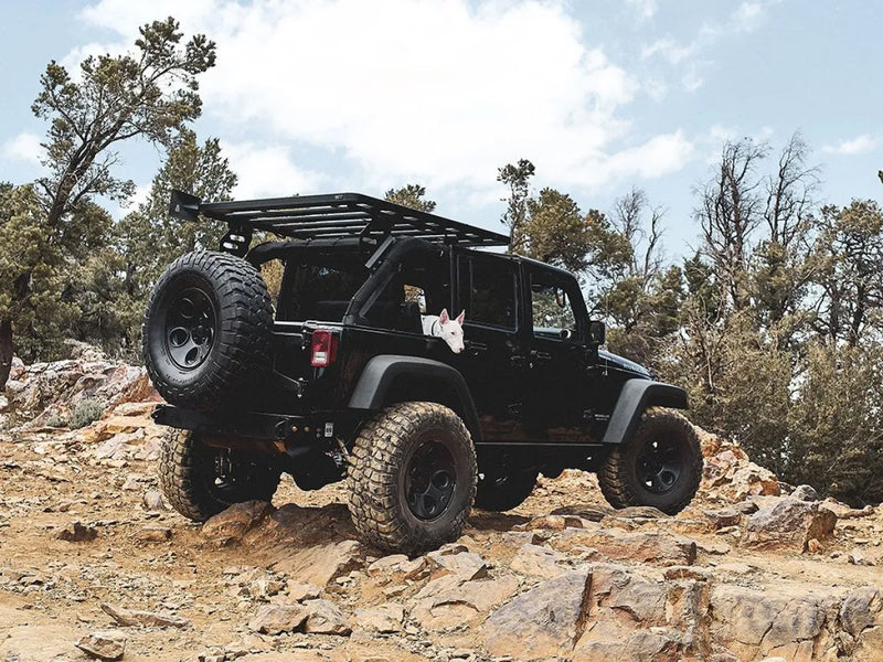 Black Jeep Wrangler with oversized tires on rocky terrain featuring Front Runner roof rack kit