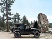 Black Jeep Wrangler with roof rack kit on dirt road showcasing Front Runner Roof Rack