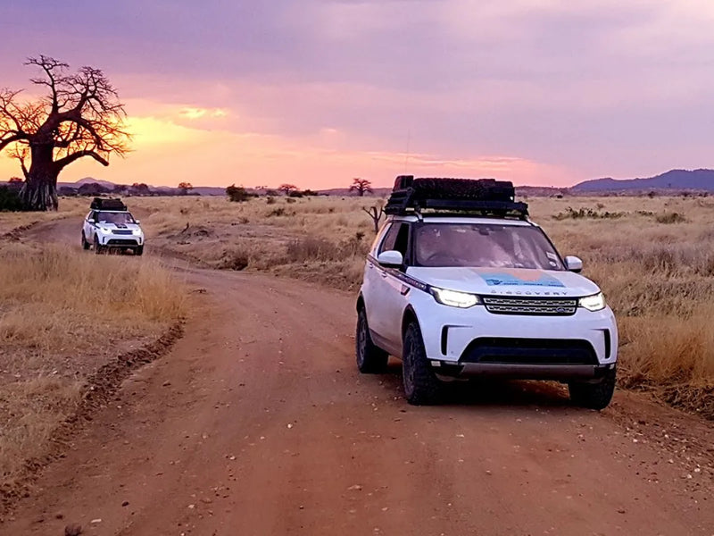 Off-road vehicles with Discovery 5 roof rack kit on dirt track in savanna at sunset