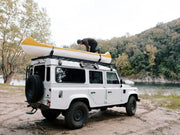 White Land Rover Defender with yellow canoe on roof rack kit for LR Defender 110