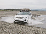 White Land Rover Discovery Sport SUV with Front Runner LR Discovery Slimline II Roof Rack Kit driving through shallow water