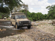 Rugged off-road vehicle with roof rack kit parked near trees and water on rocky terrain