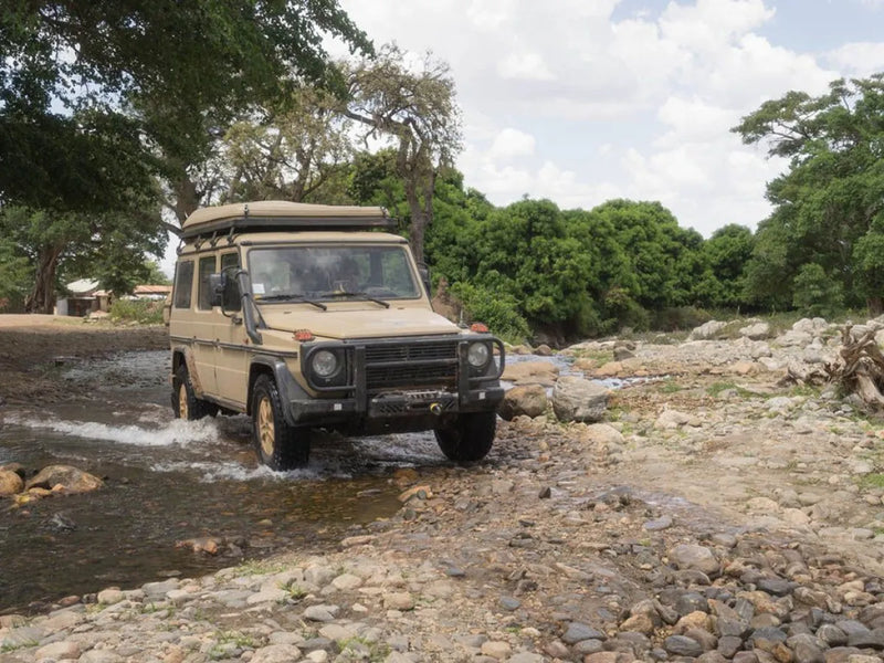Rugged off-road vehicle with roof rack kit parked near trees and water on rocky terrain