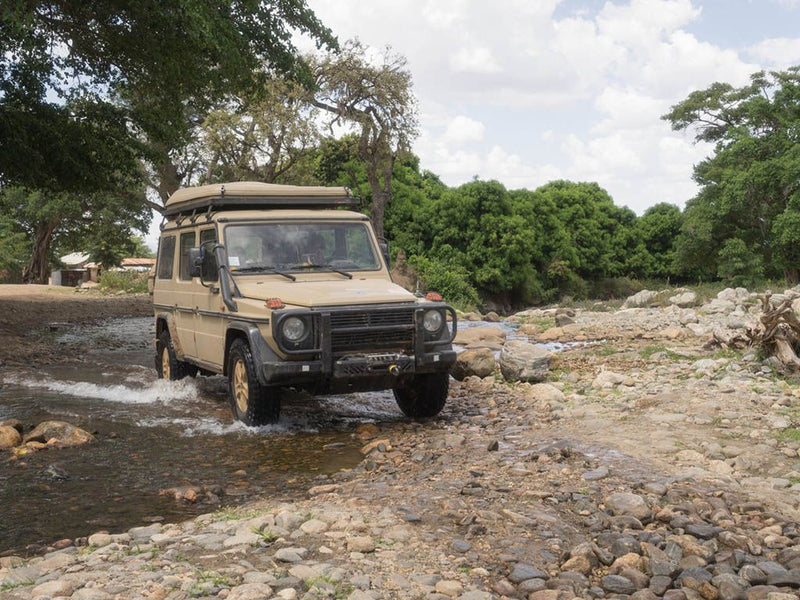 Rugged off-road vehicle with roof rack kit parked near trees and water on rocky terrain