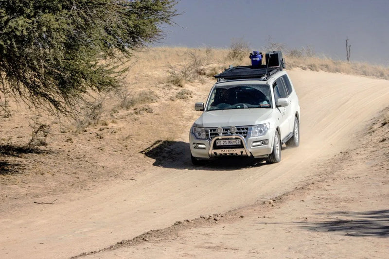 White SUV with Front Runner Mitsubishi Pajero Slimline II Roof Rack Kit driving on dusty desert road