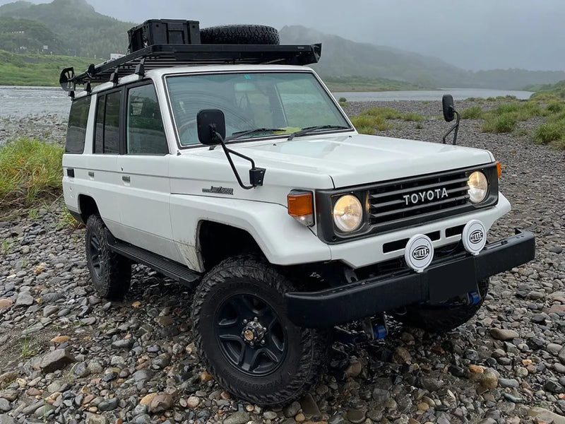 White Toyota Land Cruiser with off-road modifications featuring Front Runner Slimline II tray roof rack kit on rocky terrain