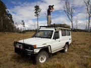 White Toyota Land Cruiser off-road with person on roof rack using binoculars in front runner roof rack kit