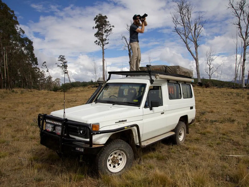 White Toyota Land Cruiser off-road with person on roof rack using binoculars in front runner roof rack kit