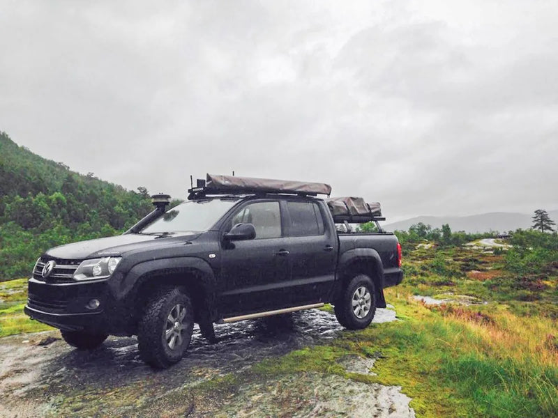 Black pickup truck with Front Runner Volkswagen Amarok Slimline II roof rack kit on rocky terrain