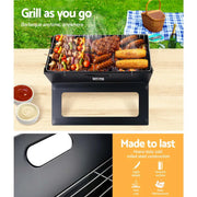 Portable charcoal bbq grill with food cooking on the grates for outdoor grilling