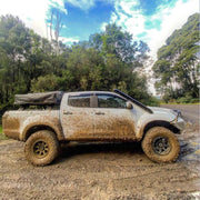 Mud-covered pickup truck with off-road tires featuring stainless steel snorkel on dirt path