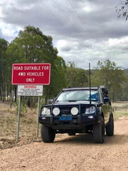 Black 4WD vehicle with stainless steel snorkel and bull bar parked on dirt road beside warning sign
