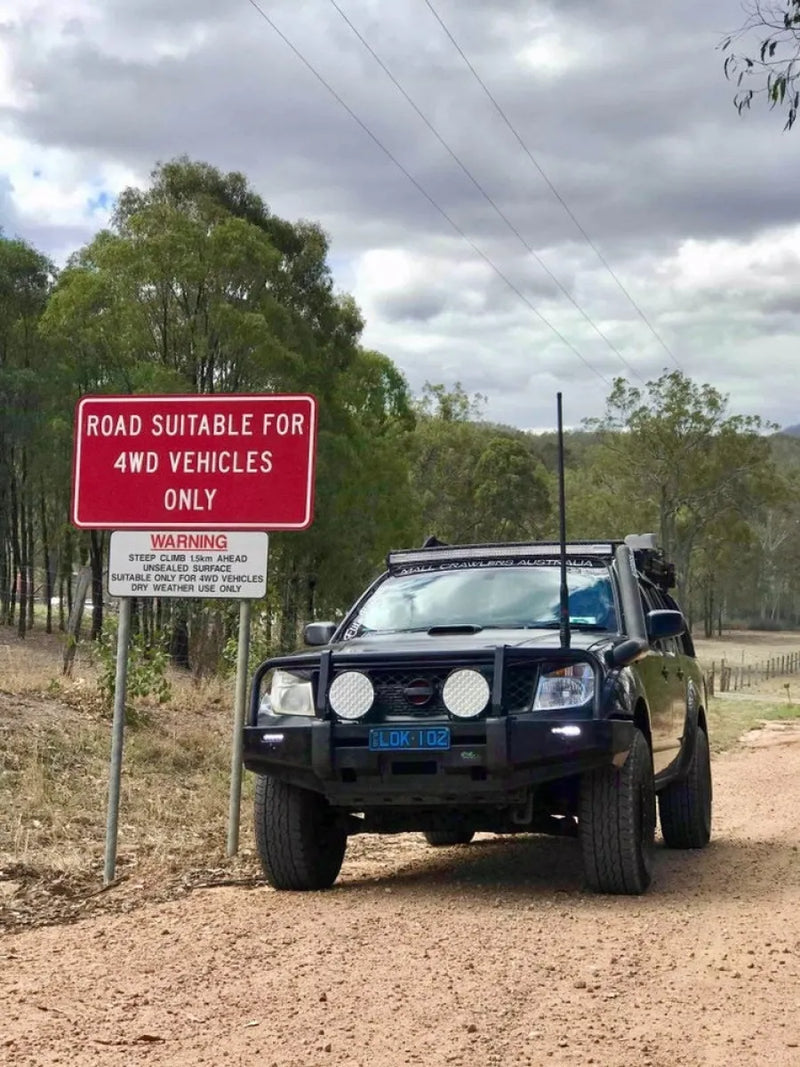 Black 4WD vehicle with stainless steel snorkel and bull bar parked on dirt road beside warning sign