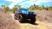 Rugged blue Nissan pickup truck with oversized off-road tires on dirt path featuring stainless steel snorkel