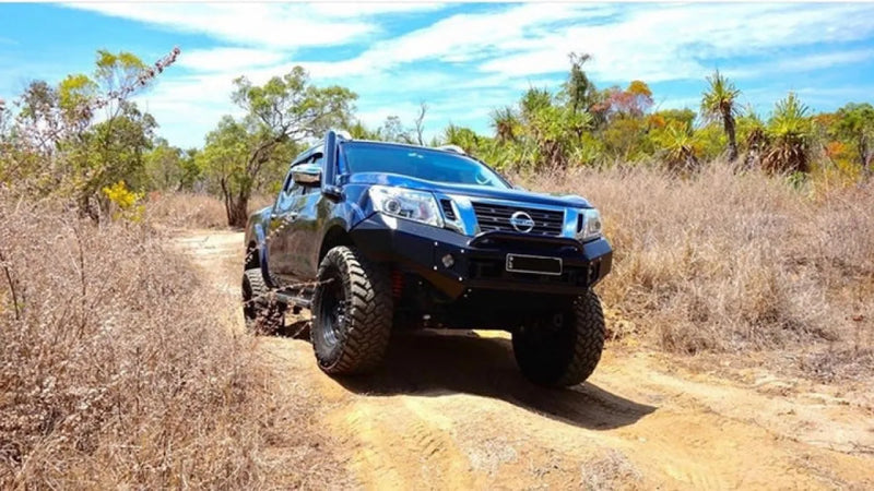 Rugged blue Nissan pickup truck with oversized off-road tires on dirt path featuring stainless steel snorkel