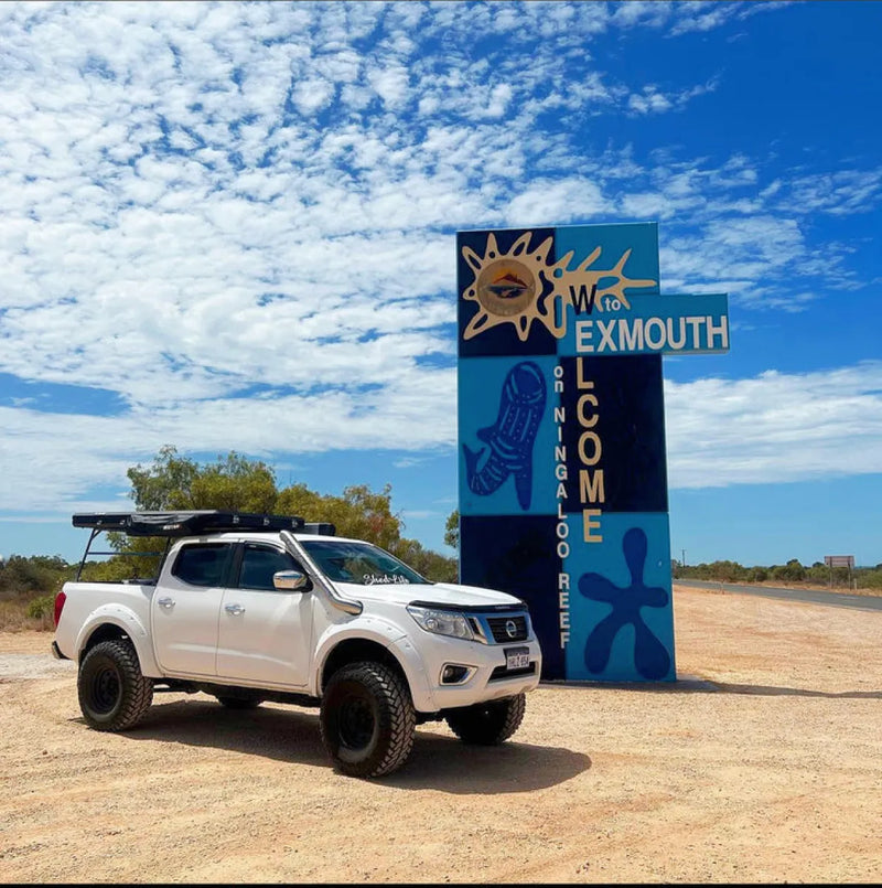 White Nissan pickup truck with stainless steel snorkel parked near colorful Exmouth welcome sign