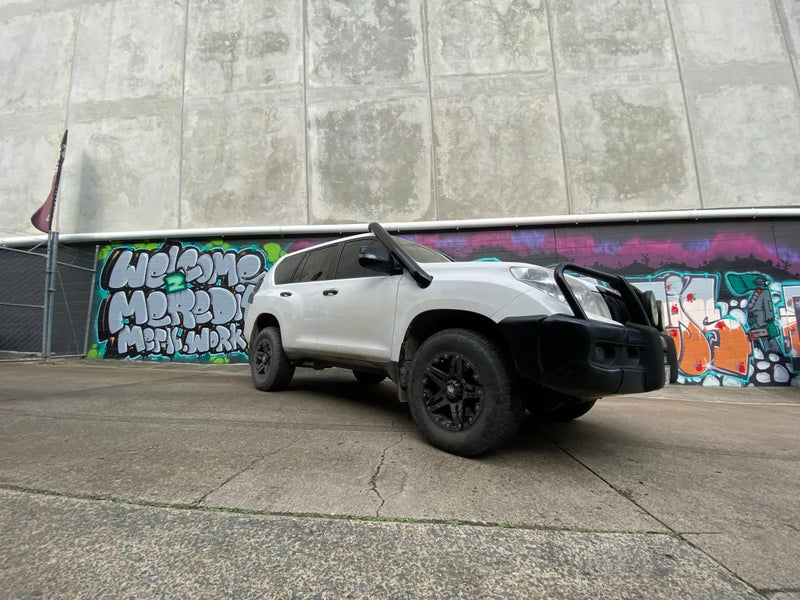 White off-road SUV with black wheels parked in front of graffiti wall showcasing stainless steel snorkel kit
