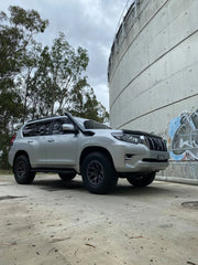 White Toyota Land Cruiser SUV with black wheels on dirt surface, equipped with stainless steel snorkel