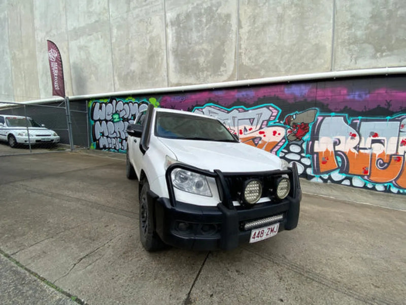 White off-road vehicle with stainless steel snorkel parked in front of graffiti wall