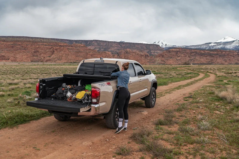 Pickup truck with UnderCover Ultra Flex hard folding tonneau cover on dirt road with camping gear