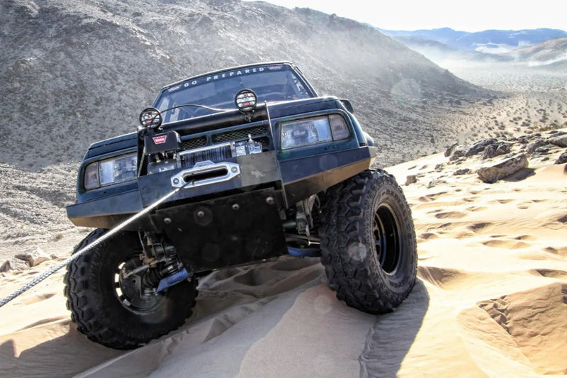 Off-road vehicle with oversized tires on rocky terrain near Warn Polished Aluminium Hawse Fairlead